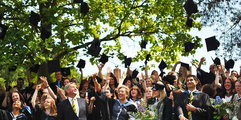 distance photograph of a university graduation day with gowns on and hats thrown in mid air