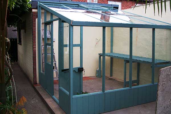 close up corner view of a lean to greenhouse constructed between a house and extension in aqua green