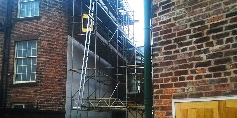 distance rear view of scaffolding between two buildings erected in such a way to allow access for people and vehicles