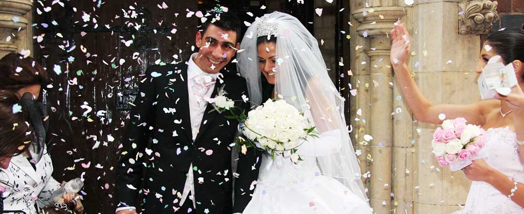 distance photograph of a just wed couple emerging from a church with confetti flying