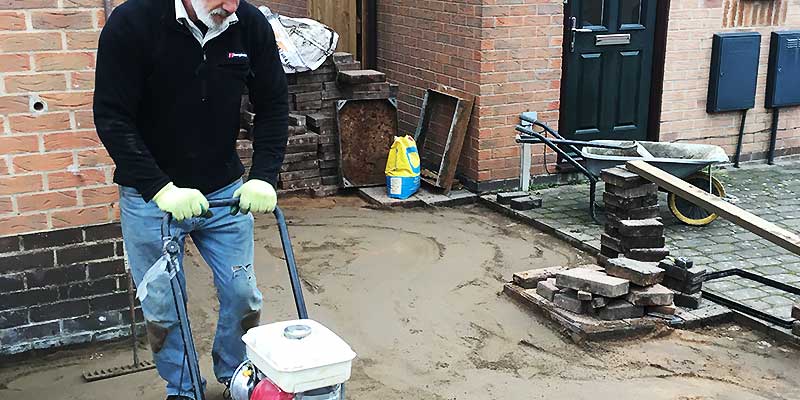 outside distance side view of russ from property maintenace finishing the base with a wacker plate ready for block paving