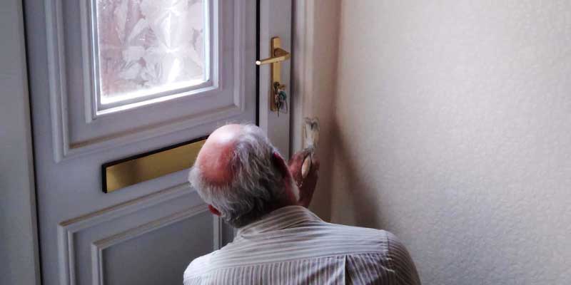 close up rear corner view of russell from property maintenance on one knee in his smart striped shirt painting a door interior frame in crisp white gloss