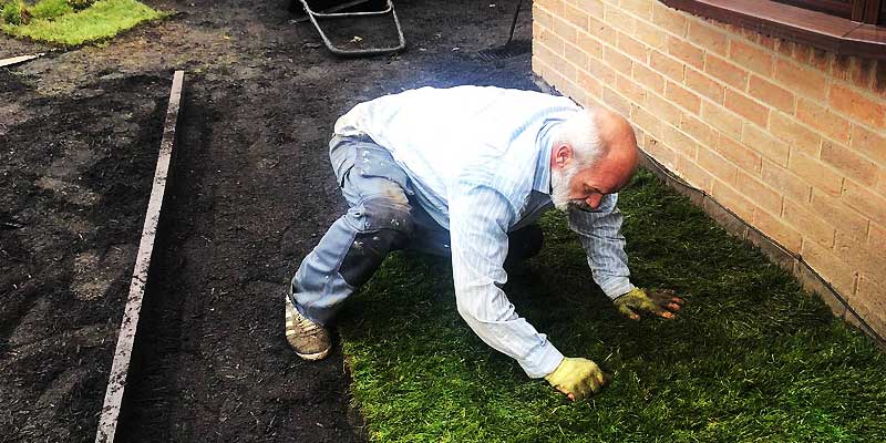 close up view of a property maintenance turf layer on his hands and knees working the turf tightly together