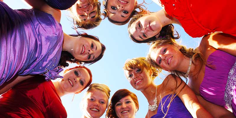 close up photograph of nine girls dressed for a birthday celebration huddled in a circle over the camera